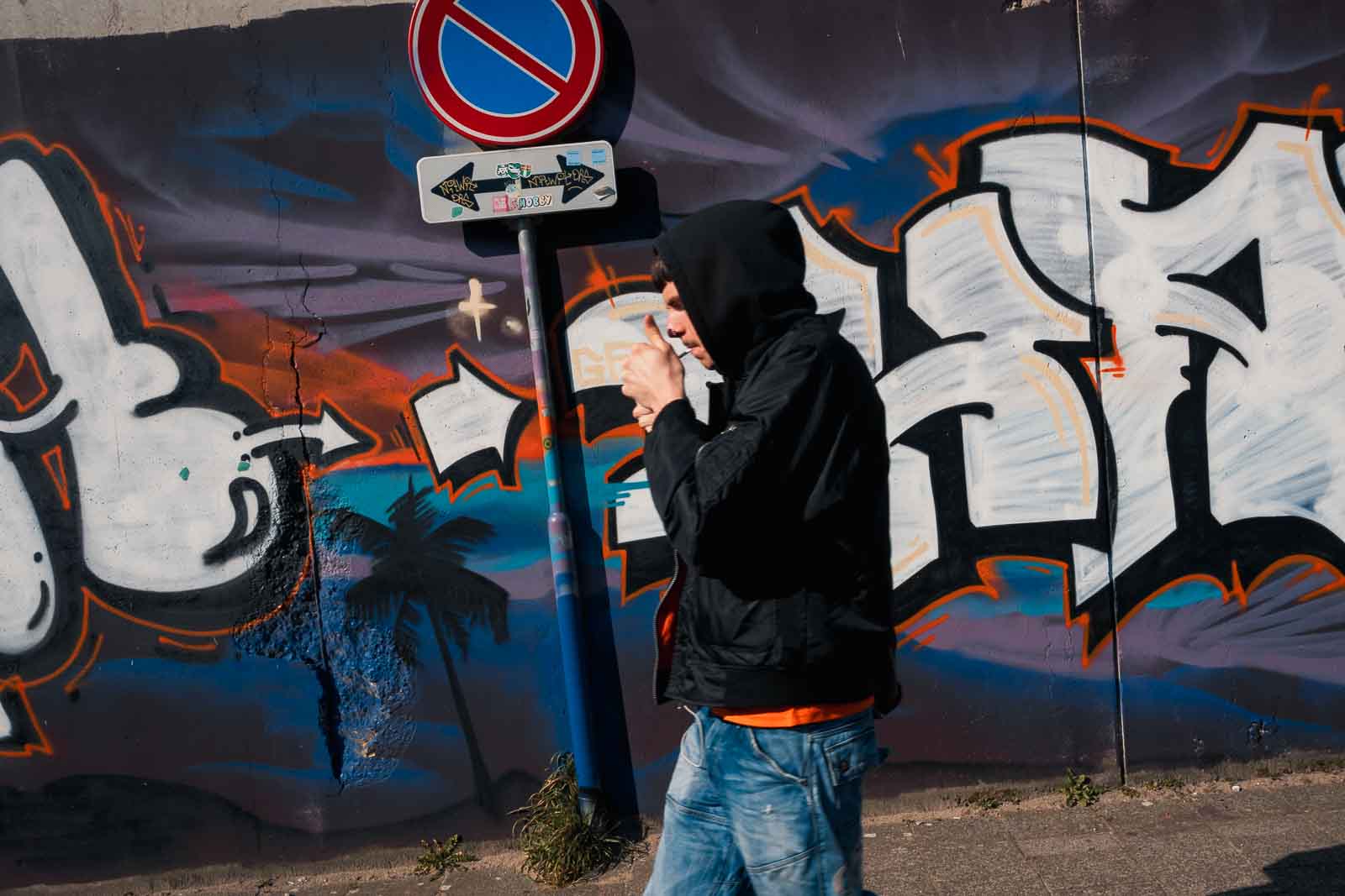 A man lighting a cigarette while standing in front of a massive, colorful street art mural in Rotterdam.