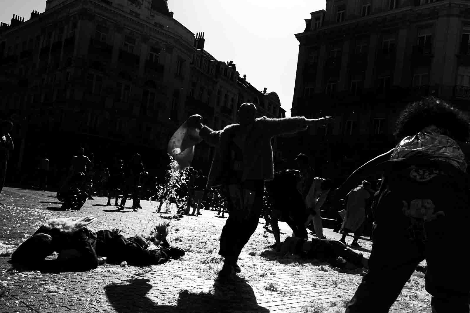 Silhouetted performers throwing pillows and feathers into the air during a dramatic street performance at the Zinneke parade in Brussels, captured in high contrast black and white.